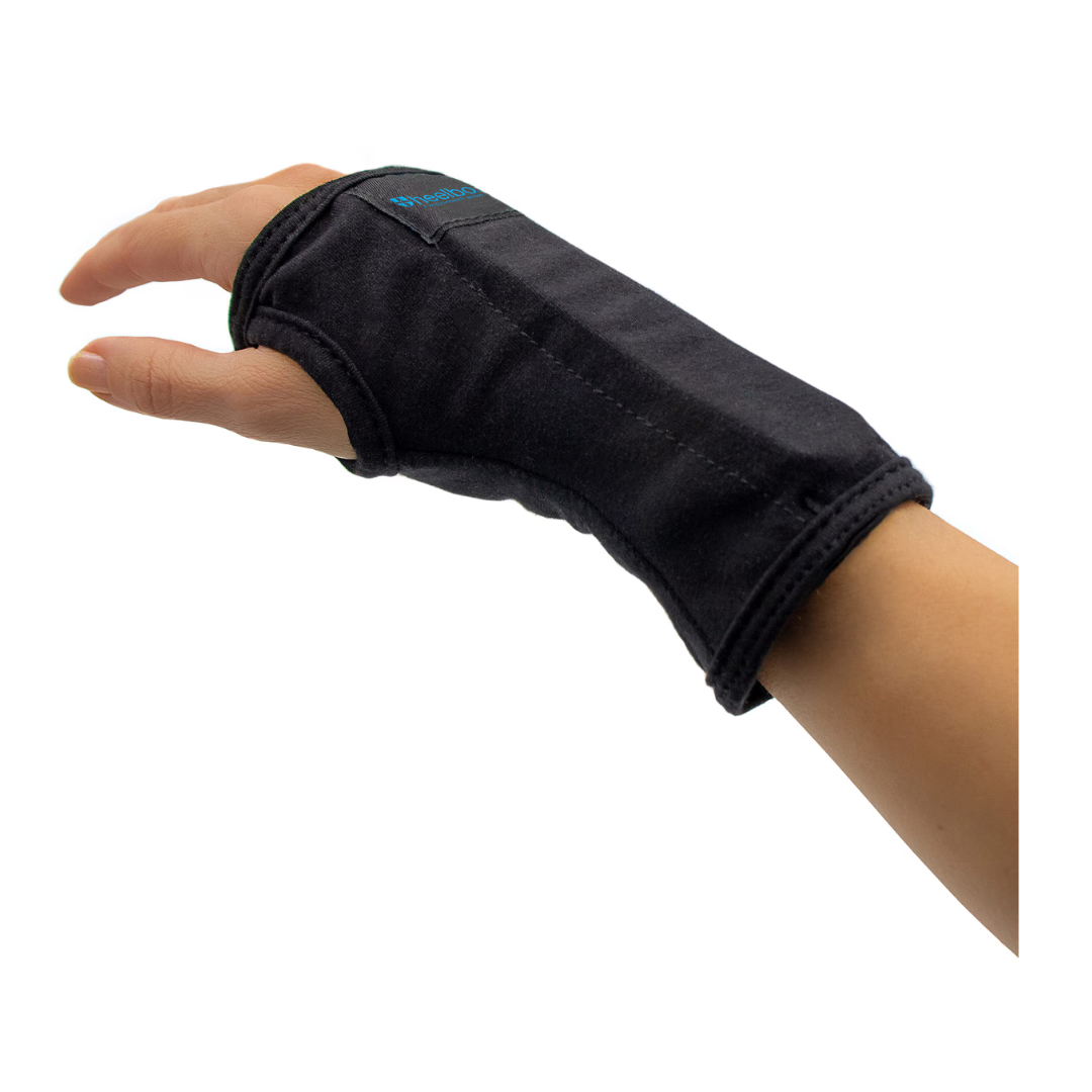 A person's left hand and wrist wearing the Heelbo Carpal Tunnel Wrist Brace—fits left & right hands—against a white background. The black brace covers the wrist and hand, leaving fingers and thumb exposed for targeted pain relief.