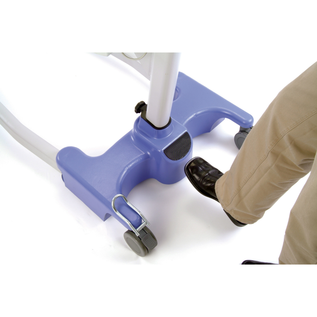A person presses a foot pedal on the Joerns Hoyer Advance Professional Electric Patient Lift, which has a blue and white base with wheels and a tapered leg design, while wearing tan pants and black shoes.