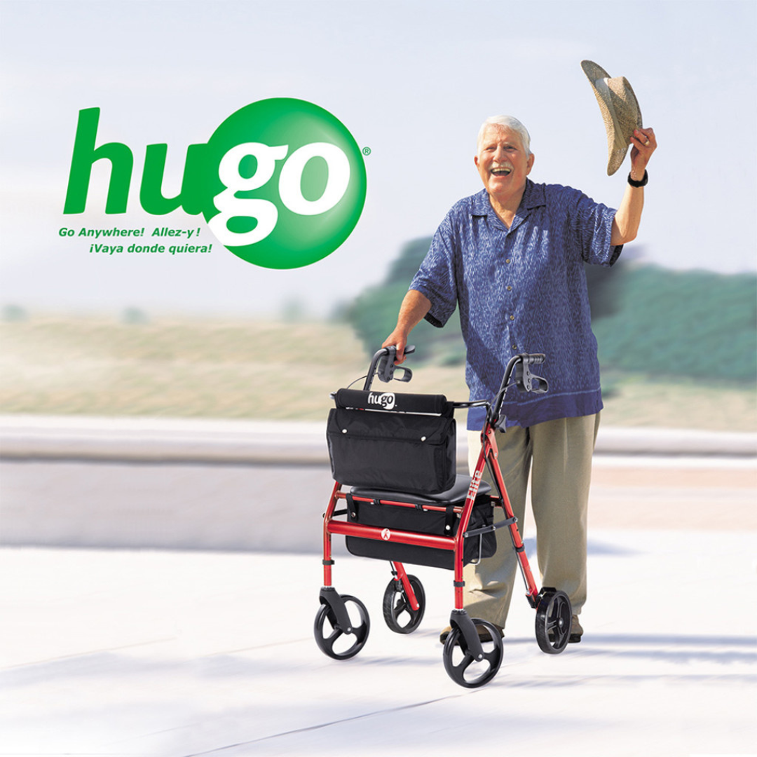 A smiling older man with white hair lifts his hat while using a Drive Hugo Elite Rolling Walker with a Seat, featuring a red frame and black bag, outdoors. The green Hugo logo and “Go Anywhere!” slogan appear in the background.