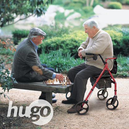 Two elderly men play chess on a garden bench, one supported by a red Drive Hugo Elite Rolling Walker with a Seat. Both smile as they enjoy the game amid lush greenery. The Hugo logo is visible in the lower-left corner.