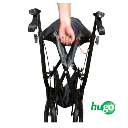 A hand grips the seat of a folded black Drive Hugo eXplore All-Terrain Side-Fold Rollator, viewed from above. The hugo logo appears in the bottom right corner.