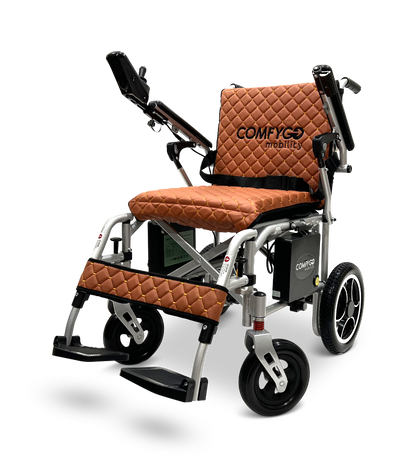 The ComfyGo X-7, a 40-lb lightweight foldable electric wheelchair, features quilted brown upholstery on the seat, backrest, and leg supports. It has foldable armrests, a right-side control panel, and large rear wheels for easy maneuverability.