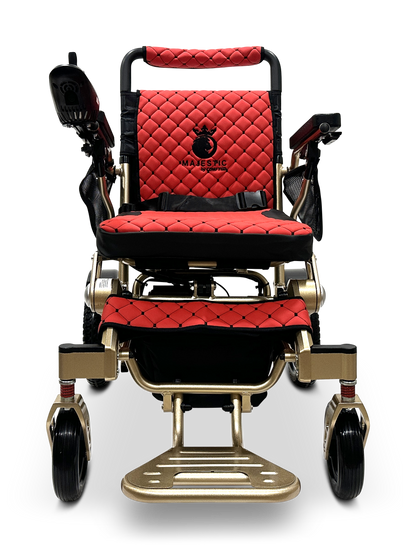 The MAJESTIC IQ-7000 Auto Folding Wheelchair features a red quilted seat with black accents, a 360-degree joystick on the right armrest, a metallic gold frame, sturdy black wheels for elegance, and the brand name Majestic on the backrest.