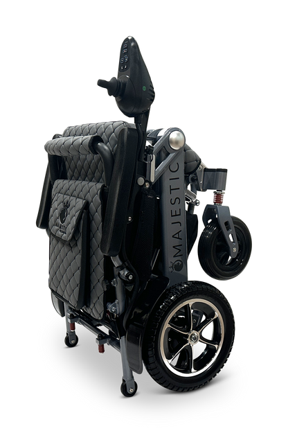 The MAJESTIC IQ-7000 Auto Folding Remote Controlled Electric Wheelchair is a compact, lightweight model with quilted fabric, black accents, a 360-degree joystick control, silver-spoked small front and larger rear wheels, and the Majestic brand elegantly displayed on the frame.