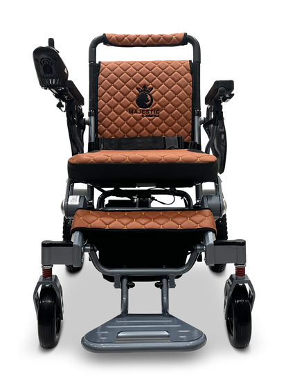The MAJESTIC IQ-7000 Auto Folding Electric Wheelchair showcases brown quilted leather seating, a sleek black control panel on the armrest, Majestic elegantly embroidered with a crown logo, and a metallic frame with black and silver accents, plus a 360-Degree Joystick for easy navigation.