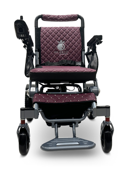 The maroon and black MAJESTIC IQ-7000 electric wheelchair features a quilted seat, backrest for comfort, armrests, 360-degree joystick on the right armrest, Majestic branding on the backrest, and a lightweight metal frame with a visible footrest.