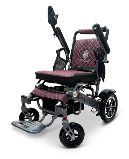 The MAJESTIC IQ-7000 Auto Folding Electric Wheelchair features a maroon, quilted seat and backrest, foldable footrest, large rear wheels, smaller front wheels, and the Majestic brand on the side. Effortless navigation is provided by its 360-degree joystick control.