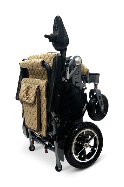 The MAJESTIC IQ-7000 is a folded electric wheelchair featuring a quilted tan seat, black frame, and 360-degree joystick on the armrest. It has small front wheels, larger rear wheels with silver rims, and is set against a sleek black background.