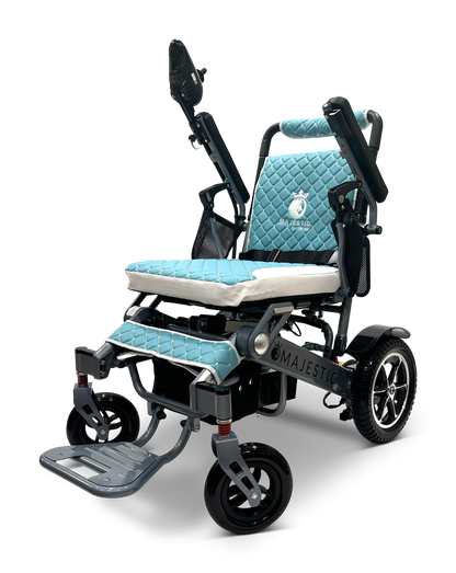 The MAJESTIC IQ-7000 is a lightweight, auto-folding electric wheelchair featuring a blue quilted seat and backrest, large rear wheels, smaller front wheels, armrests, and a 360-degree joystick. The brand name Majestic is visible on the frame.