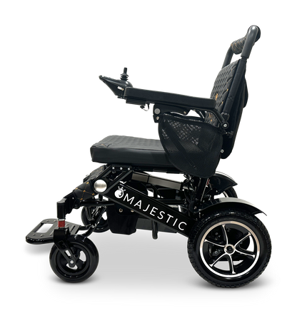 Side view of the MAJESTIC IQ-7000 Remote Controlled Electric Wheelchair in black with the brand name displayed on its frame. It includes a cushioned seat, joystick control on the armrest, and sturdy wheels suitable for various terrains. Despite its robust construction, this lightweight wheelchair is versatile and placed against a plain black background.