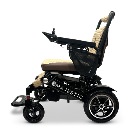 Side view of a beige and black MAJESTIC IQ-7000 Remote Controlled Electric Wheelchair, featuring a cushioned seat, a joystick for control, and rugged wheels designed for comfort and mobility. This lightweight wheelchair offers exceptional convenience without compromising durability.