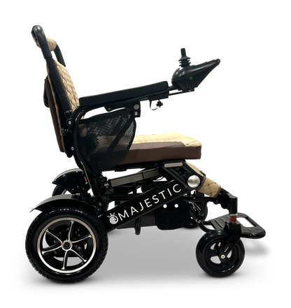 Side view of the lightweight black and beige MAJESTIC IQ-7000 Remote Controlled Electric Wheelchair, featuring a joystick control on the armrest. The Majestic brand name is displayed on the frame, and this innovative model offers an auto-folding feature for added convenience.