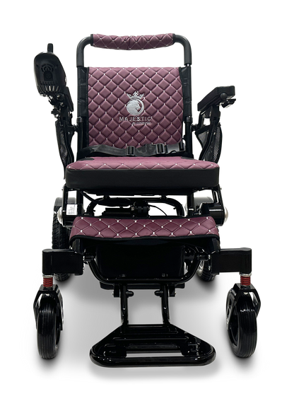 A front view of the MAJESTIC IQ-7000 Remote Controlled Electric Wheelchair showcases its sleek, black folding design with quilted maroon cushioning. The backrest displays an emblem reading "Majestic." It is equipped with an intelligent joystick on the left armrest and large front wheels for enhanced stability.