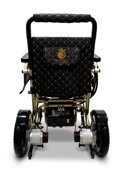 Introducing the MAJESTIC IQ-7000 Remote Controlled Electric Wheelchair, featuring a black and gold design with quilted seat upholstery. It showcases a logo with a crown and the word "Majestic." This lightweight travel wheelchair is equipped with large rear wheels, smaller front wheels, and a 360-degree intelligent joystick for effortless mobility.