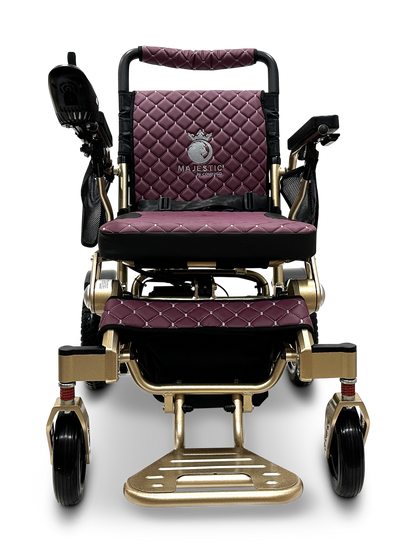 Introducing the MAJESTIC IQ-7000 Remote Controlled Electric Wheelchair, a luxurious folding wheelchair with a quilted burgundy cushion and a golden frame adorned with the Majestic logo. It features supportive armrests, a footrest, and large rear wheels to enhance mobility.
