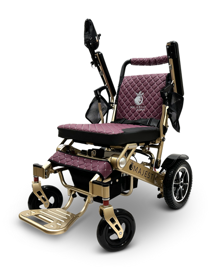 The MAJESTIC IQ-7000 Remote Controlled Electric Wheelchair boasts a luxurious design with quilted burgundy cushions and a golden frame. It features a joystick control on the armrest, a footrest, and sturdy wheels, proudly displaying "Majestic" on its side.