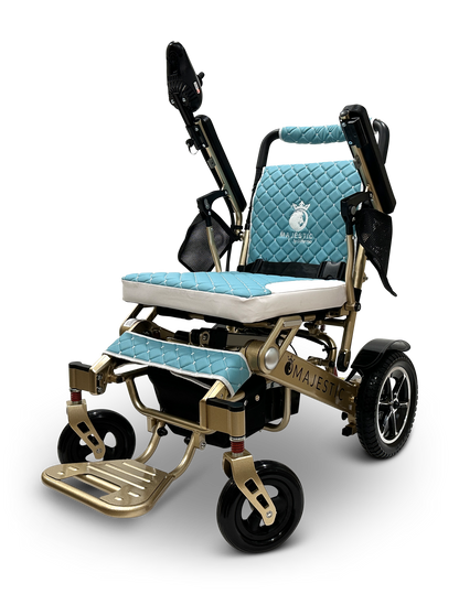 The gold-colored MAJESTIC IQ-7000 auto-folding electric wheelchair features turquoise quilted cushions, black armrests, large rear wheels, smaller front wheels, a 360-degree joystick, and a footrest. The brand name Majestic is prominently displayed on the side.