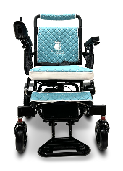 The MAJESTIC IQ-7000 Remote Controlled Electric Wheelchair is equipped with a comfortable, blue quilted seat complete with armrests, footrests, and a joystick control on the left arm. The seat and backrest showcase a white logo displaying the text MAJESTIC. This wheelchair features a sleek black frame paired with four wheels to ensure smooth maneuverability.