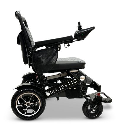 Side view of a black MAJESTIC IQ-7000 Remote Controlled Electric Wheelchair with the name etched on the frame. It is equipped with a cushioned seat, armrests, and a joystick for navigation. The folding wheelchair design showcases two large rear wheels and smaller front wheels.