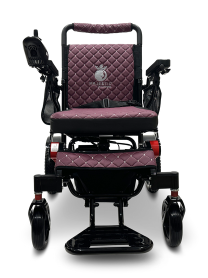 Introducing the MAJESTIC IQ-7000 Remote Controlled Electric Wheelchair: a lightweight, purple electric mobility chair with a diamond-patterned design. It features padded armrests and joystick control for ease of use. The Majestic brand name is elegantly embroidered on the backrest. With a sleek black frame and caster wheels, this auto-folding model combines convenience and style effortlessly.