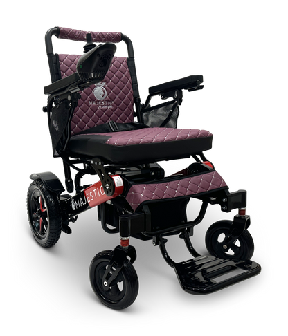The MAJESTIC IQ-7000 Remote Controlled Electric Wheelchair is a maroon and black lightweight model with quilted upholstery and armrests. It features an intelligent joystick for seamless control, with four wheels providing stability. The brand name Majestic is prominently displayed on the side of this auto-folding electric wheelchair, combining convenience and style in one elegant package.