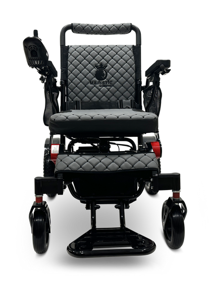 The MAJESTIC IQ-7000 Remote Controlled Electric Wheelchair is a sleek black model with an auto-folding feature and a quilted seat and backrest. It includes comfortable armrests, intelligent joystick control on the right side, and smaller front wheels. The brand logo is prominently displayed on the backrest.