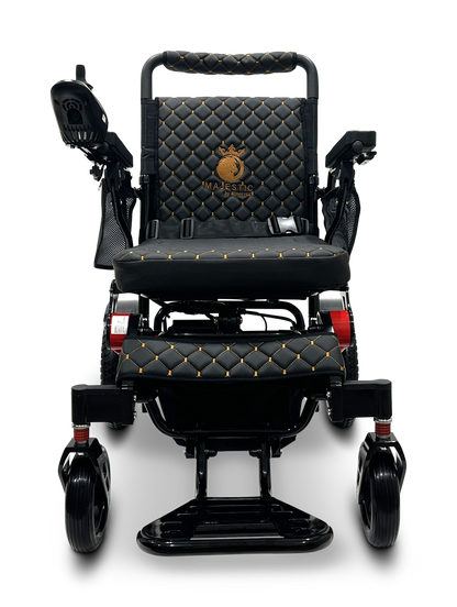 Introducing the MAJESTIC IQ-7000 Remote Controlled Electric Wheelchair: a luxurious black and gold mobility aid with quilted leather upholstery and adjustable armrests. It features an intelligent joystick conveniently located on one armrest for enhanced ease of use, while its auto-folding capability adds to the convenience of this lightweight wheelchair, ensuring both comfort and style in motion.