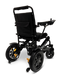 The ComfyGo MAJESTIC IQ-9000 Auto Folding Electric Wheelchair is a stylish, black mobility device with a digital joystick controller for precise navigation. It includes a cushioned seat and backrest, robust rear wheels powered by brushless silent motors, and smaller front wheels. The wheelchair also features armrests and a storage pocket on the back.