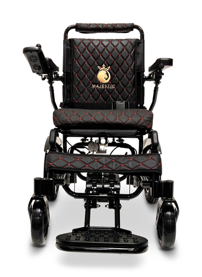 The ComfyGo MAJESTIC IQ-9000 Auto Reclining Electric Wheelchair features a black quilted seat and backrest with red stitching, aircraft-grade aluminum alloy frame, armrest controls, and a gold Majestic crown logo on the backrest.