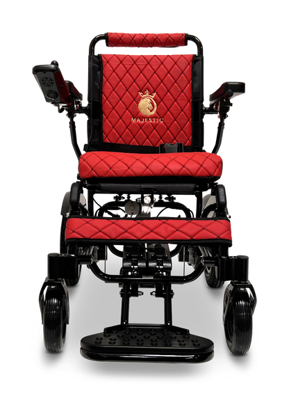 A front view of the ComfyGo MAJESTIC IQ-9000 Auto Reclining Electric Wheelchair in red and black, featuring quilted upholstery, armrests, a left-side digital joystick controller, and Majestic branding with a gold horse logo on the backrest.