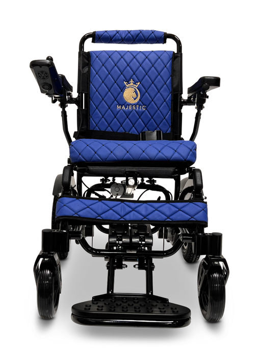 The ComfyGo MAJESTIC IQ-9000 Auto Folding Electric Wheelchair is available in black and blue, featuring brushless silent motors and a quilted pattern on the seat and backrest. The word "MAJESTIC" is embroidered on the backrest with a decorative logo above it. This model includes a digital joystick controller for seamless navigation.