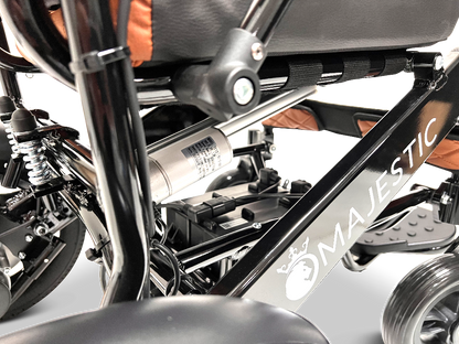 Close-up of the ComfyGo MAJESTIC IQ-9000 Auto Reclining Electric Wheelchair, showing its aircraft-grade aluminum alloy frame, suspension, battery compartment, digital joystick controller, and seat with orange accents.