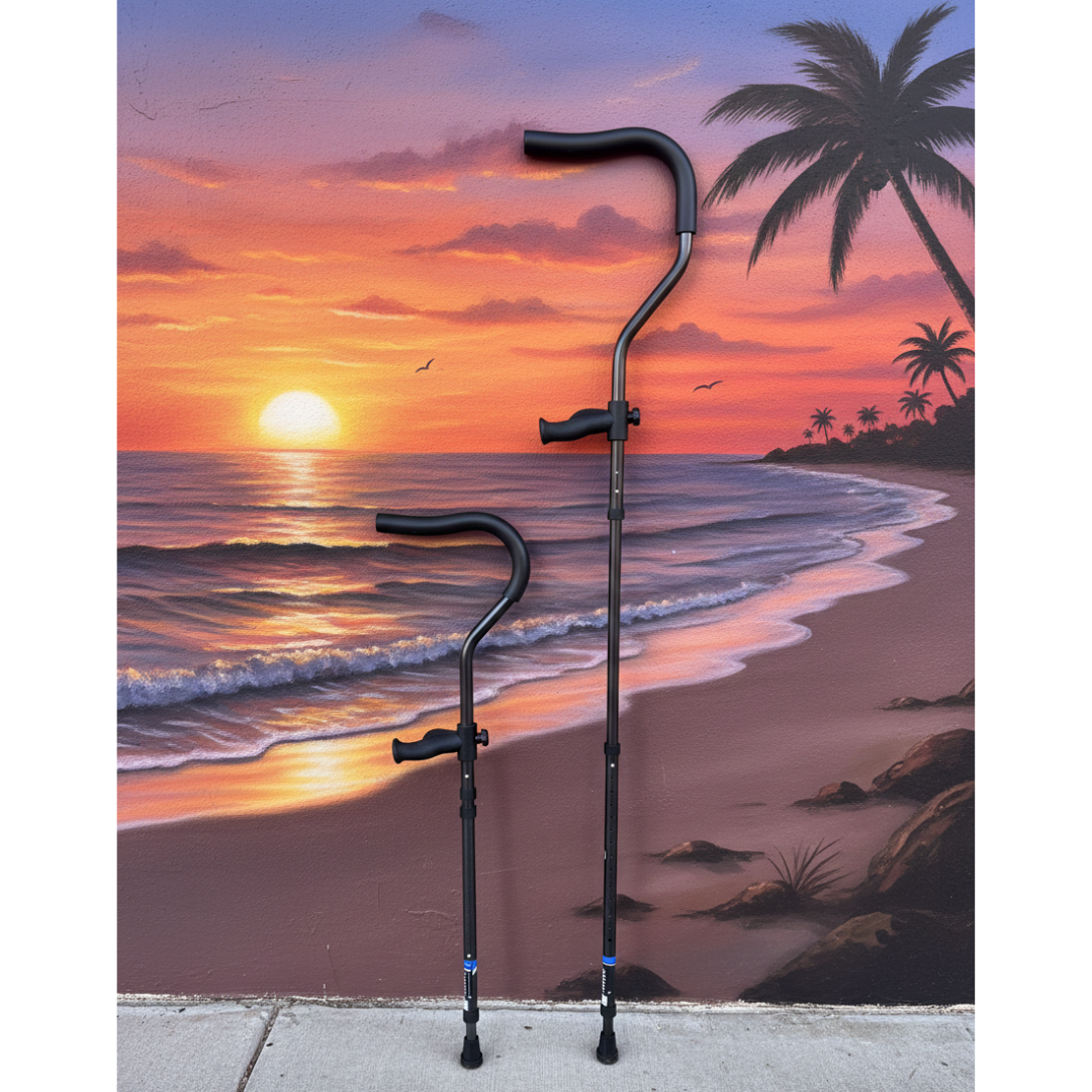 Two Millennial Medical In-Motion Pro Underarm Folding Crutches stand upright on a sidewalk before a vibrant mural of a tropical beach sunset, featuring waves, palm trees, birds, and an orange-purple sky.