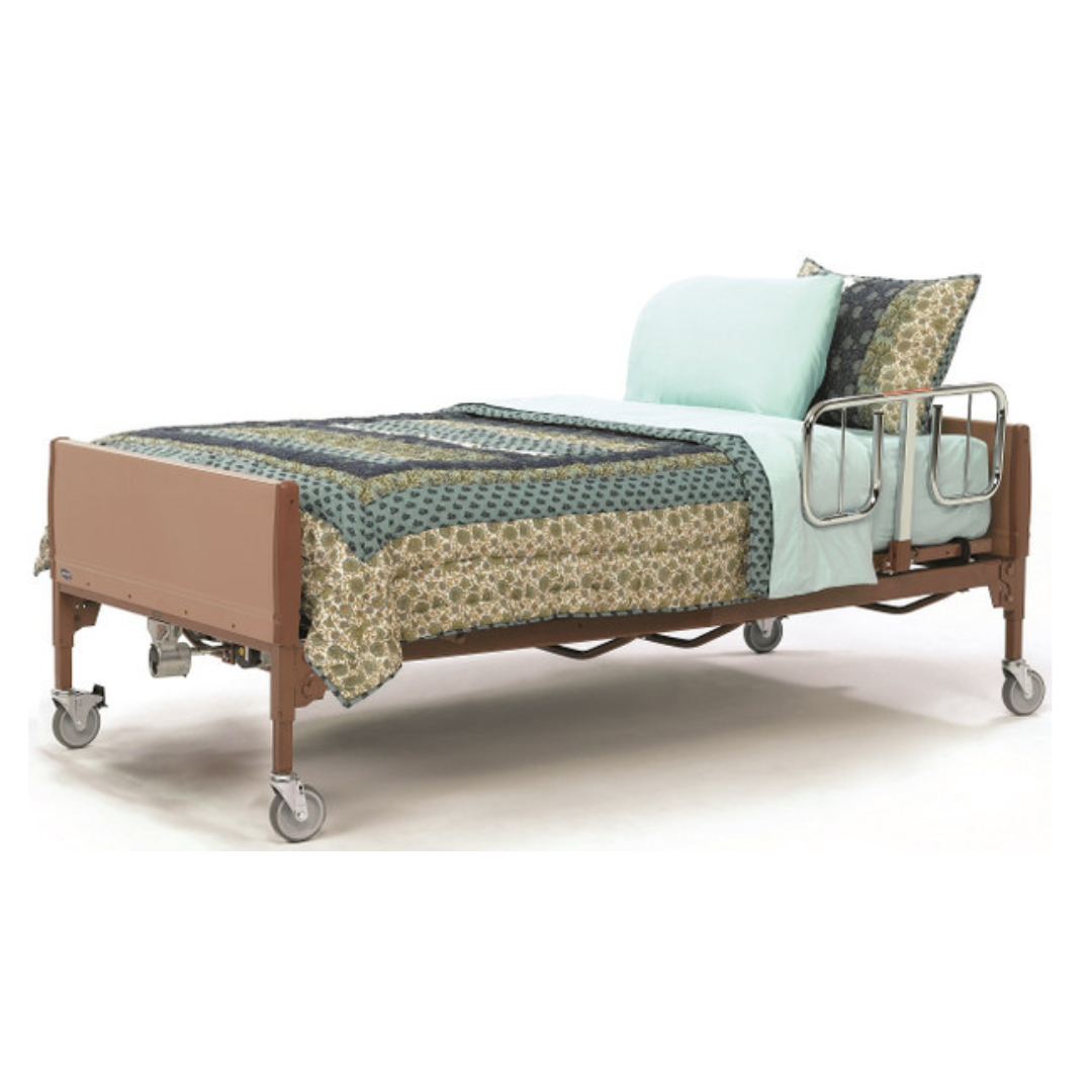 The Invacare Full-Electric BAR600 Bariatric Homecare & Hospital Bed, featuring wheels and metal side rails, is topped with a patterned quilt, light blue blanket, and pillows, and is angled against a plain white background.