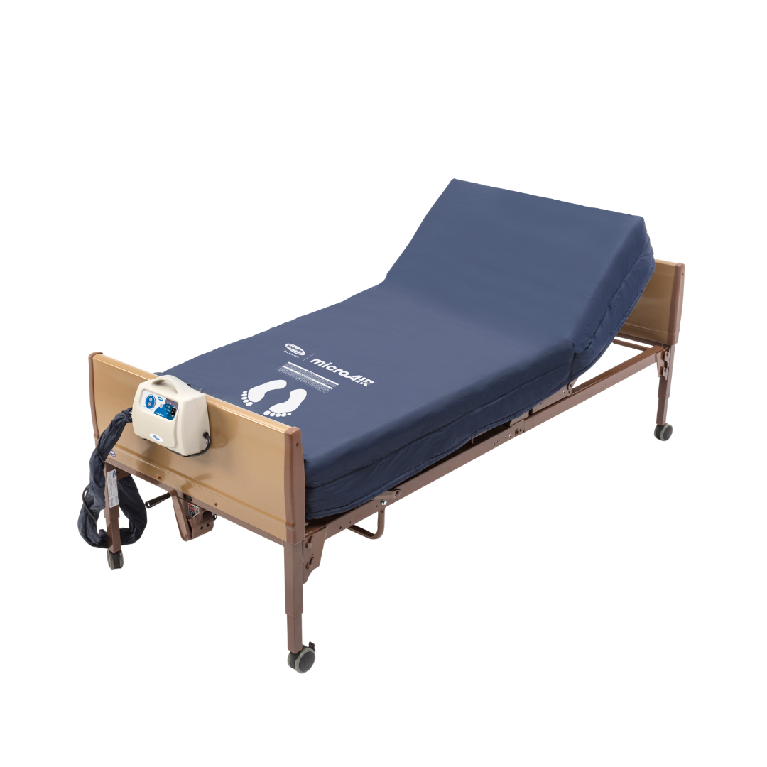 A hospital bed with an Invacare microAIR® MA500 Alternating Pressure Low Air Loss Mattress System in blue, featuring an electronic control unit at the foot, light brown rails, wheels, and shown partially elevated.