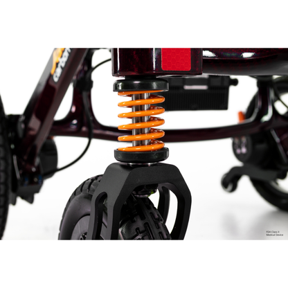 Close-up of the Pride Jazzy Carbon HD Bariatric Portable Powerchair’s front wheel and orange suspension spring, showcasing its durable wheel and suspension system against a white background.