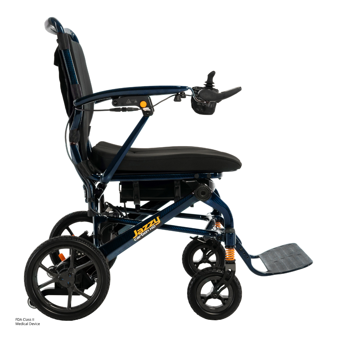 A side view of the Pride Jazzy Carbon HD Bariatric Portable Powerchair in blue, featuring a black seat, armrests, joystick controller, footrest, four wheels, and the word "Jazzy" on the frame near the rear wheels.