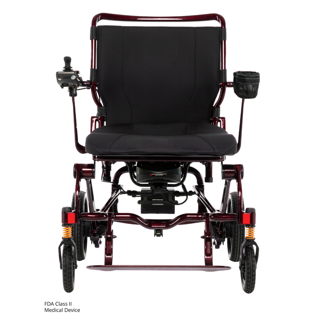Front view of the Pride Jazzy Carbon HD Bariatric Portable Powerchair in red, featuring a black cushioned seat, armrests, left-side joystick control, right-side cup holder, and suspension springs above the front wheels.