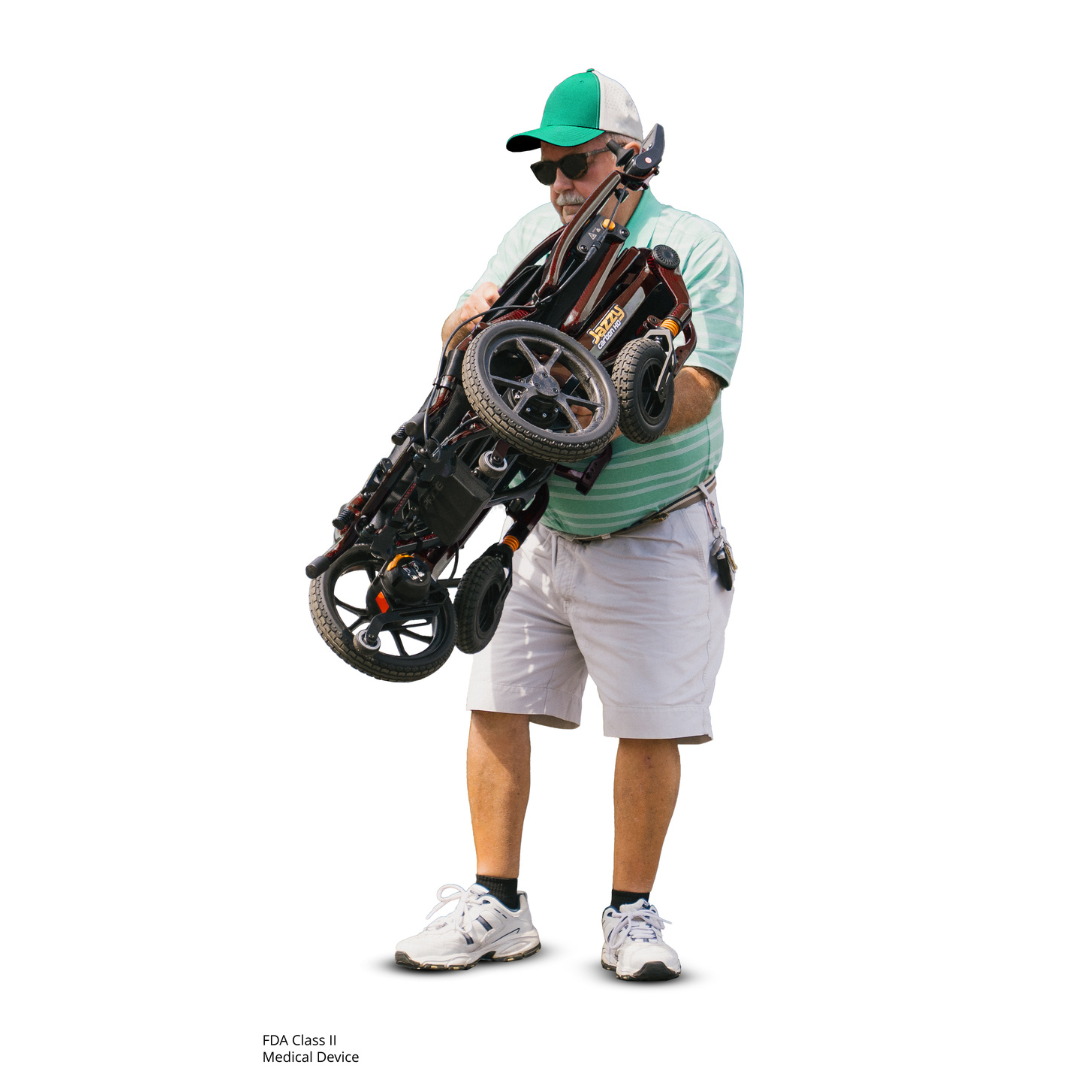 A man in sunglasses, a green cap, green-striped polo, and khaki shorts carries a folded Pride Jazzy Carbon HD Bariatric Portable Powerchair against a plain white background.