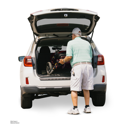 An older man in a cap, striped shirt, and shorts loads a folded Pride Jazzy Carbon HD Bariatric Portable Powerchair into the trunk of a white SUV with its rear hatch open.