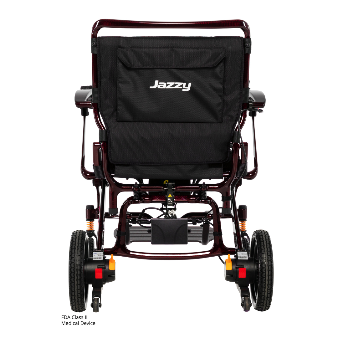 Rear view of the Pride Jazzy Carbon HD Bariatric Portable Powerchair, showing large rear wheels, smaller front wheels, Jazzy branding on the backrest, and visible mechanisms under the seat.