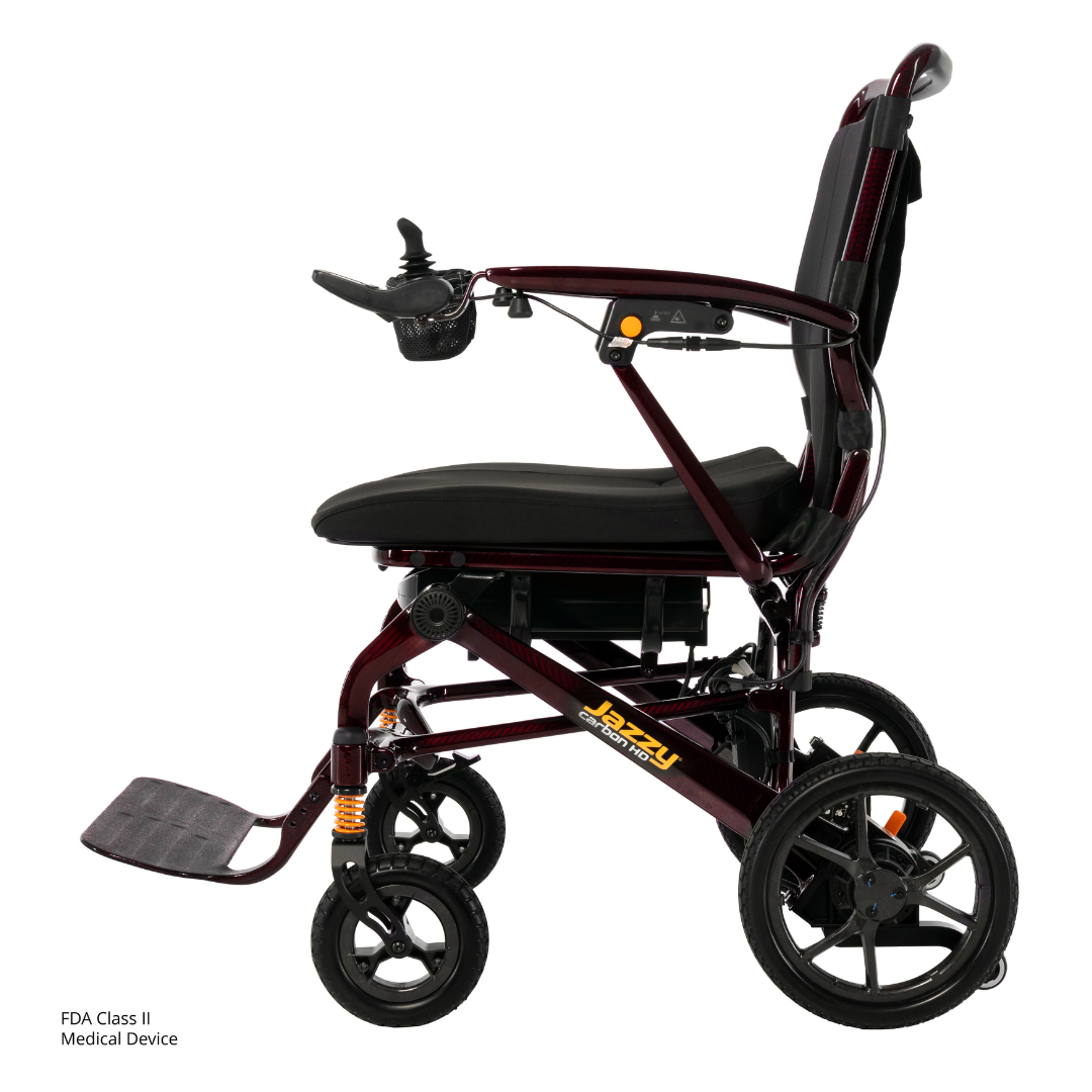 Side view of a maroon Pride Jazzy Carbon HD Bariatric Portable Powerchair with a black seat, armrests, right-arm joystick control, large rear wheels, small front casters, and a lightweight foldable frame.
