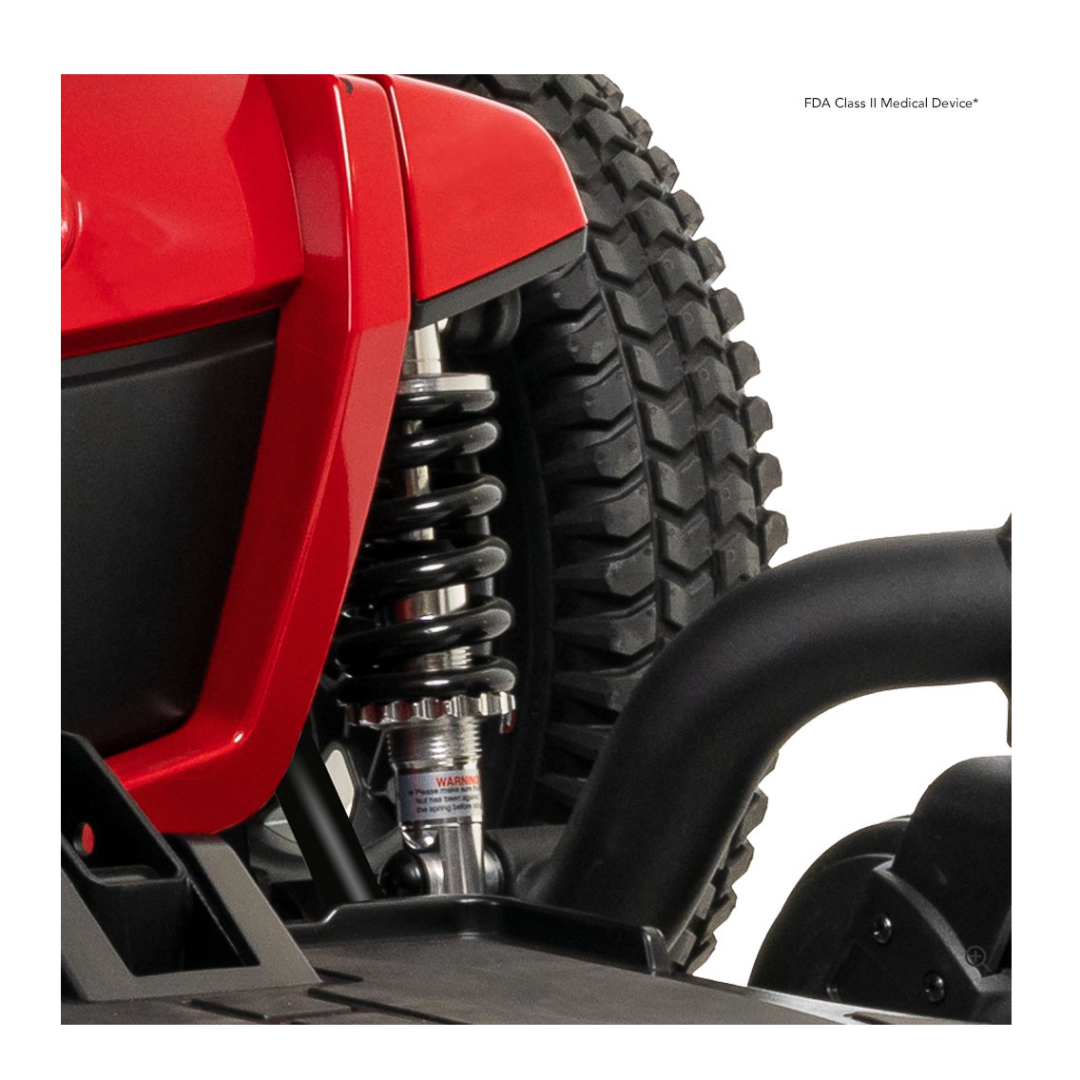 Close-up of the Pride Mobility Jazzy® 600 ES Powerchair with ATX Suspension, showing the rear suspension spring, part of a large treaded tire, and black frame. FDA Class II Medical Device text is visible in the top right corner.