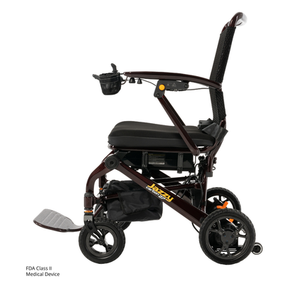 The Jazzy® Carbon 27 Ultralite Portable Power Wheelchair is a lightweight, foldable carbon fiber chair with a black seat, side armrests, footrest, small front wheels, large rear wheels, cup holder, storage pouch, and is an FDA Class II medical device.