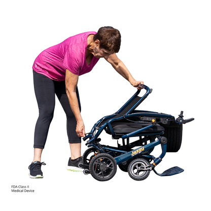A woman in athletic wear bends down to fold or adjust a Jazzy® Carbon 27 Ultralite Portable Power Wheelchair against a white background.