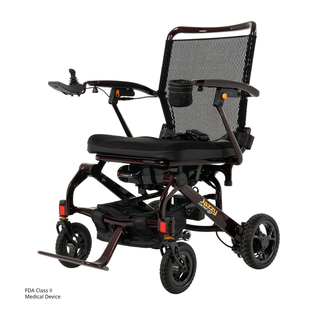 The Jazzy® Carbon 27 Ultralite Portable Power Wheelchair features a lightweight, foldable carbon fiber frame, black mesh seat and backrest, armrests, right-side joystick controller, four wheels, and footrests—perfect for travel.