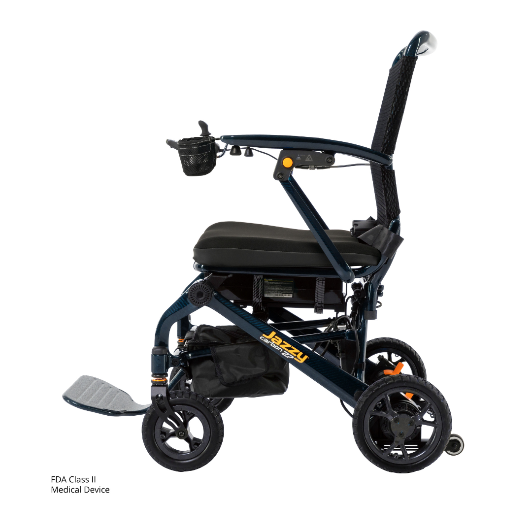 The Jazzy® Carbon 27 Ultralite Portable Power Wheelchair features a lightweight, foldable carbon fiber frame in black, cushioned seat, armrests, footrest, under-seat storage bag, and a right armrest cup holder for convenience.