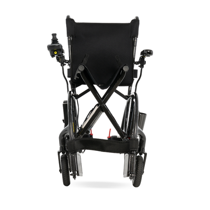 A rear view of the Pride Jazzy® Carbon 27X Portable Power Wheelchair, folded for easy transport or storage, featuring ultra-lightweight design, sturdy wheels, and a joystick controller on the left armrest.