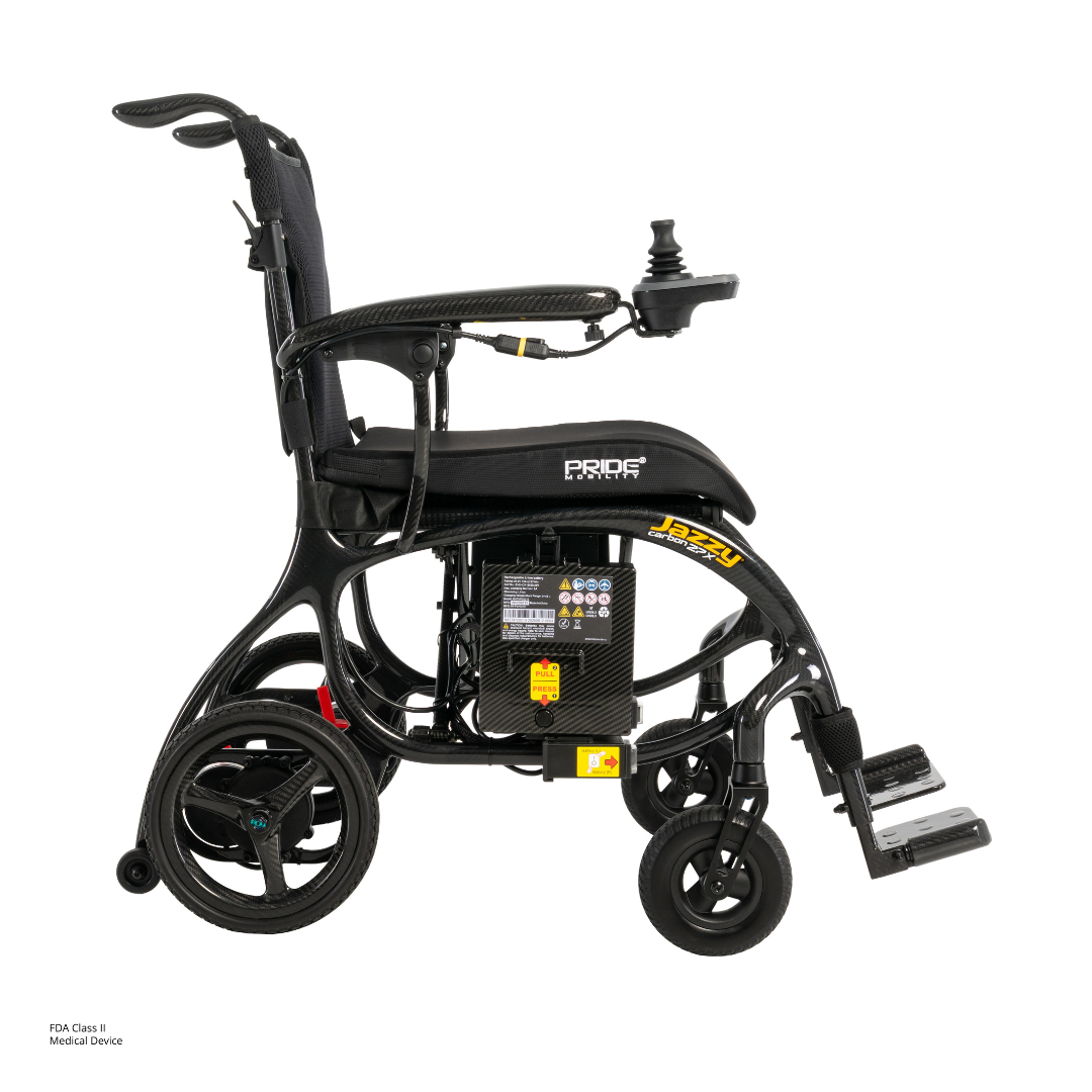 The Pride Jazzy® Carbon 27X Portable Power Wheelchair, shown in black with rear wheels, footrests, and armrest joystick control visible against a plain white background. The Pride Mobility logo appears on the side.