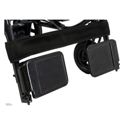 Close-up of two black rectangular footplates with a mesh strap above them, attached to the frame and small wheels of the Pride Jazzy® Carbon 27X Portable Power Wheelchair.